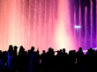 © schankz - Silhouettes of people at a colored fountain at night.