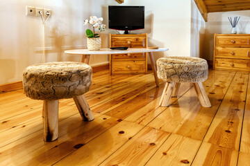 Part of living room. Two small three leged backless stools with on the wooden floor, at the  background TV set and table. Interior design. 