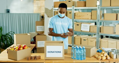 Wall Mural - African American young handsome happy male warehouse worker volunteer working in shipping delivery charitable stock organization packing donations box Donating and volunteering, charity center concept