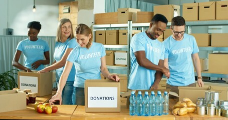 Wall Mural - Mixed-race happy positive male and female different volunteers working in charity organization center preparing and packing social help box, donations box, volunteering and donating concept