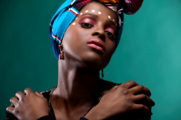 African American dark skinned black woman is wearing a traditional cultural ethnic head wrap. she poses in the studio is glamour cosmetic makeup and fashionable clothes 