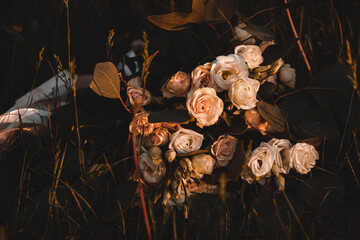 A bouquet of chic white and beige roses tied with a white ribbon lies on the grass in the light of the sun at sunset.