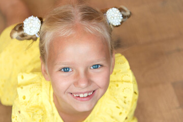 cute little blonde with bright emotions - a wide smile with open teeth. She is wearing a simple yellow dress. European race.