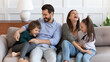 © fizkes - Overjoyed young Caucasian family with children have fun tickle play together in cozy modern living room. Happy parents feel playful enjoy funny game with kids relaxing together at home on weekend.