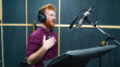 © Nik Viatkin - Expressive bearded man with curly ginger hair in headphones at recording studio stay opposite a microphone and performs like voice actor