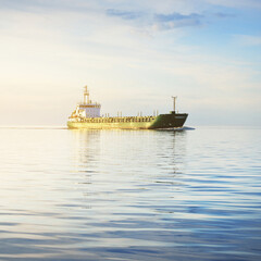 Large green cargo ship sailing in an open sea at sunset. Colorful glowing clouds, warm sunlight. Concept image. Freight transportation, business, economy, industry, global communications, logistics