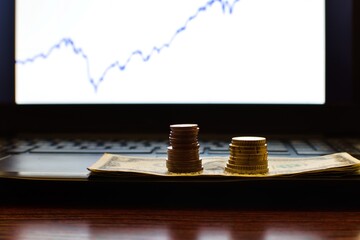 stacks of coins on dollars on blurred computer screen background with stock chart