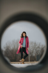 Canvas Print - Full body shot of a beautiful cool woman wearing a pink coat posing in a snowy park through a hole