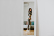 © shevtsovy - Fitness Woman Measuring body With Tape Standing In Front Of Mirror At Home. Beautiful woman checking success of weight loss program and measuring butt in front of mirror in living room. Slimming