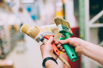 A man in a hardware store holds a set of brushes and rollers for paint and decor.