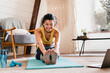 © InsideCreativeHouse - Cheerful african sporty girl stretching on the mat at home. Black fitness woman exercising at laptop having online training at home. Stay fit concept