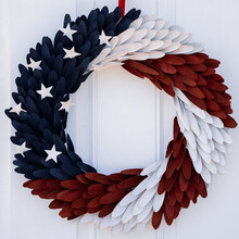 Photograph Of A Red, White And Blue Door Wreath With Stars Symbolizing An American Flag Hung On A White Door