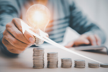 businessman hand holding light bulb with coins stacking on the desk. saving energy and money, the idea with innovation and inspiration concept saving energy and money