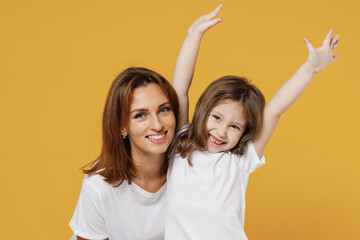 Happy woman in basic white t-shirt have fun cute child baby girl 5-6 years old raised hands up. Mommy little kid daughter isolated on yellow color background studio. Mother's Day love family concept.