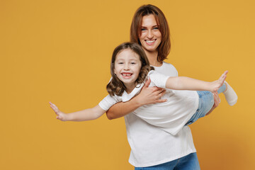 Wall Mural - Happy woman in basic white t-shirt have fun hold cute child baby girl 5-6 years old fly. Mommy little kid daughter isolated on yellow orange color background studio. Mother's Day love family concept.