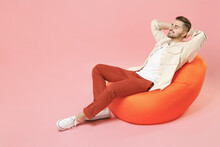 Full Length Young Smiling Happy Overjoyed Joyful Fashionable Man 20s In Jacket White T-shirt Sitting In Bean Bag Chair Resting Hold Hand Behind Neck Isolated On Pastel Pink Background Studio Portrait