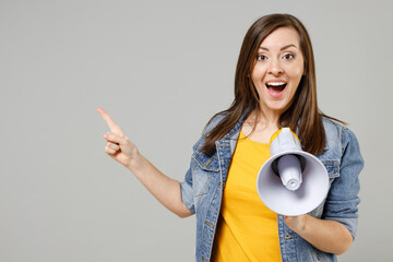 Wall Mural - Side view young caucasian woman 20s wear casual trendy denim jacket yellow t-shirt screaming aside shouting in megaphone point index finger aside on workspace area isolated on grey background studio