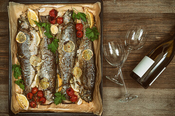 Roasted trout with vegetables on a baking sheet and two wineglass with  white wine.Rustic food photography.Flat lay.