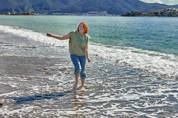 Wall Mural - Young woman walks barefoot on beach in surf zone.