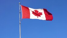 Canadian Flag Blowing In The Wind With Clear Blue Sky And Snow Flakes; Slow Motion