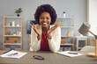 © Studio Romantic - Happily smiling satisfied african american woman worker sitting at table in office looking at camera holding palms up headshot portrait. Funny conversation or successful interview online. Webcam view