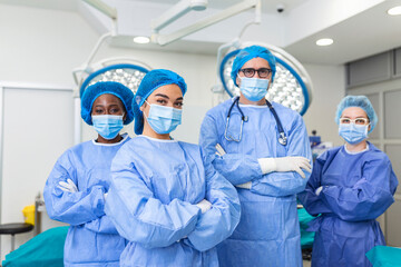 Wall Mural - multi-ethnic group of four healthcare workers, a team of doctors, surgeons and nurses, performing surgery on a patient in a hospital operating room. They are looking at the camera.