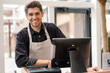 © Drobot Dean - Smiling young man in apron standing at the cash register