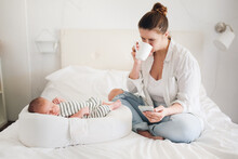 Cute Caucasian Mom With A Newborn Baby. Mother With Phone And Coffee While Baby Is Sleeping, Concept Of Motherhood, Social Networks And Communication Of Mom In Decree