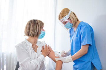 Closeup of a nervous woman and her doctor wearing face masks and getting a vaccine shot in a doctor's office. Woman get vaccinated during pandemic times.