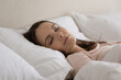 © fizkes - Relaxed calm girl sleeping peacefully in soft linen comfortable bedding, lying on orthopedic mattress with head resting on pillow, smiling with closed eyes. Young woman enjoying bedtime recreation
