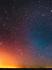 Wall Mural - Amazing Night Sky Glowing Stars Background Backdrop In Rotation. Colorful Sky Gradient. Sunset Sunrise Light And Colourful Night Starry Sky In Blue Yellow Pink Orange Colors. Dark Ground Silhouette