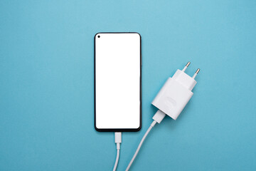 Smartphone charging connection via USB cable and power supply on a blue background. Smartphone with a white screen. top view, business and technology. copy space. Flat lay. mockup