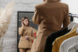 © triocean - Young woman choosing clothes and trying on beige blazer in fashion atelier or personal wardrobe.