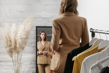 Young Woman Choosing Clothes And Trying On Beige Blazer In Fashion Atelier Or Personal Wardrobe.