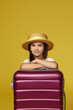 child with pink suitcase on yellow background.