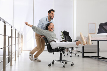 Wall Mural - Office employee giving his colleague ride in chair at workplace