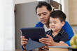 © DragonImages - Father showing educational video to his excited smiling little son when they are sitting at kitchen table