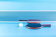 Two table tennis or ping pong rackets and balls on a baby blue table with net.