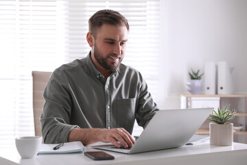 Wall Mural - Young man working on laptop at table in office