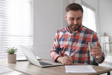 Wall Mural - Young man with glass of water working at table in office