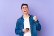 © luismolinero - Teenager caucasian  handsome man isolated on purple background with phone in victory position