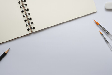Wall Mural - open blank spiral notebook with paintbrush, pencil and eraser on white background, empty space for y