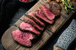 Sliced grilled marbled meat steak Filet Mignon, with onion and asparagus, on wooden serving board, with meat knife and fork, on black wooden table background