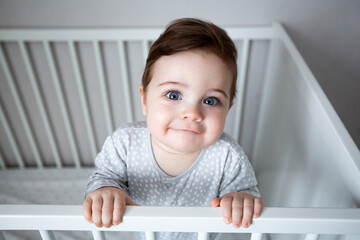 Funny little baby boy with beautiful blue eyes standing in a white crib