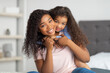 © Prostock-studio - Love between parent and child. Positive little black girl hugging her mom on bed at home