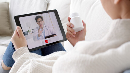 Wall Mural - Over shoulder view of young asia woman talk to doctor on cellphone videocall conference medical app in telehealth telemedicine online service hospital quarantine social distance at home concept.