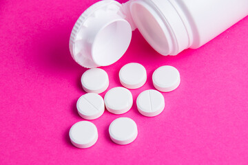 White pills and jar on pink paper background copy space top view.