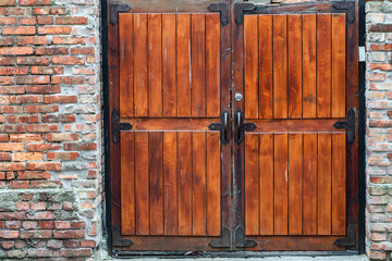 Red painted wooden barn door and window in old brick wall