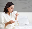 © chadchai - Asian woman in a bathrobe enjoys having morning tea on bed.