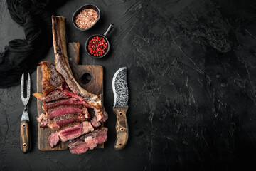 Wall Mural - Sliced barbecued tomahawk rib tip with rosemary, salt and herbs medium rare, on wooden serving board, on black stone background, top view flat lay, with copy space for text